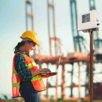 Young engineer woman standing wear safety helmet working with work by laptop evening time. blur background, concept of renewable energy and clean power.